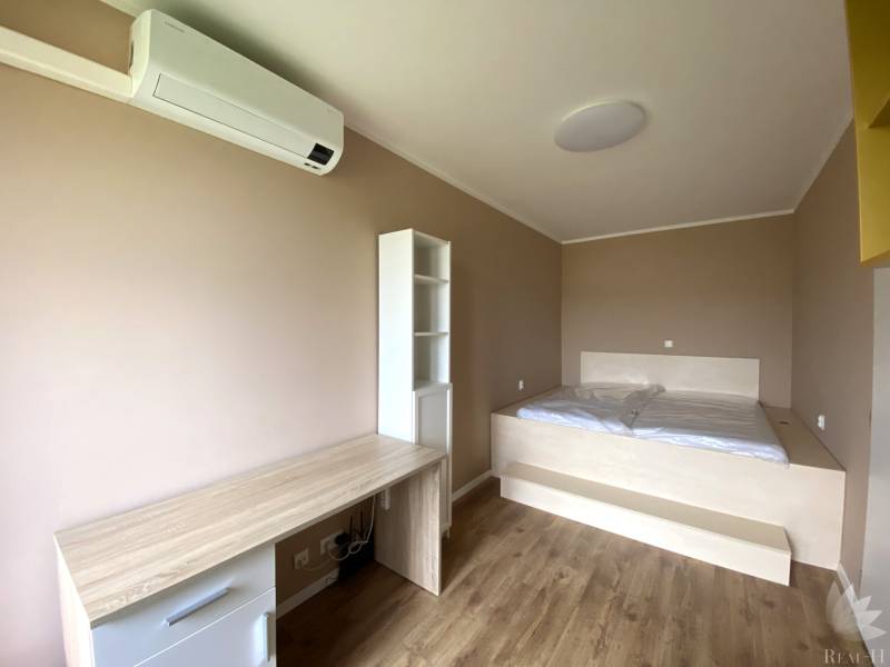 Bedroom in a 3-room apartment with wood-patterned flooring, a bed, and a desk.