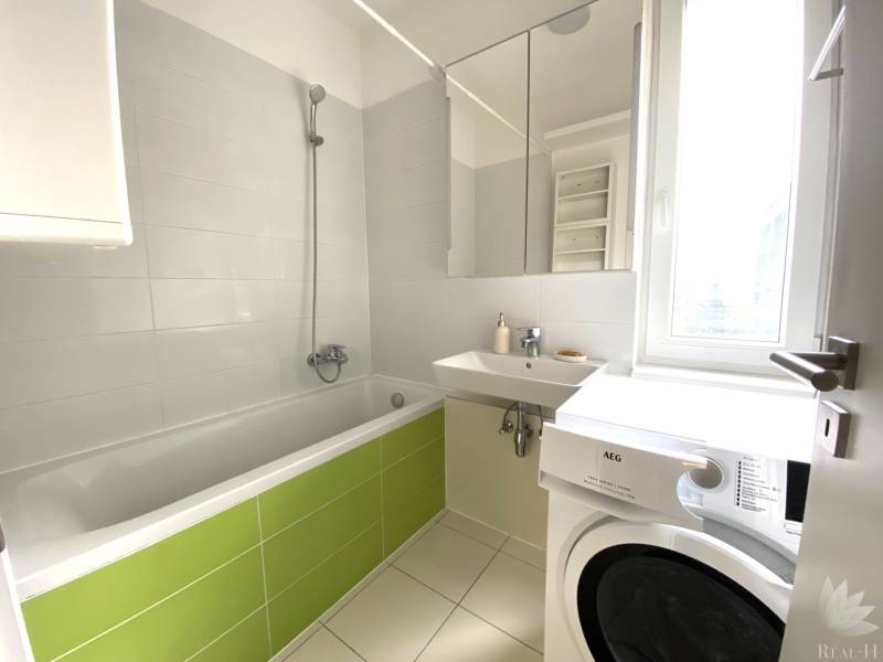 A bathroom with a shower, bathtub, sink, and washing machine in a 3-room apartment.