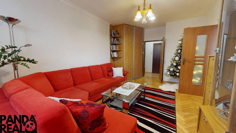 Living room in a 3-room apartment with a red sofa, a fir tree, and a floor with a wooden decor.