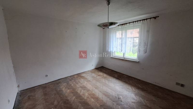 An empty room with a window, chandelier, and wooden-patterned floor in a family house.