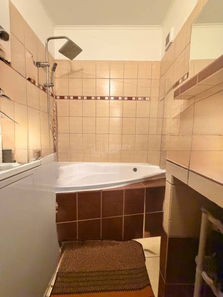 A bathroom in a 2-room apartment with a corner bathtub and beige tiles.