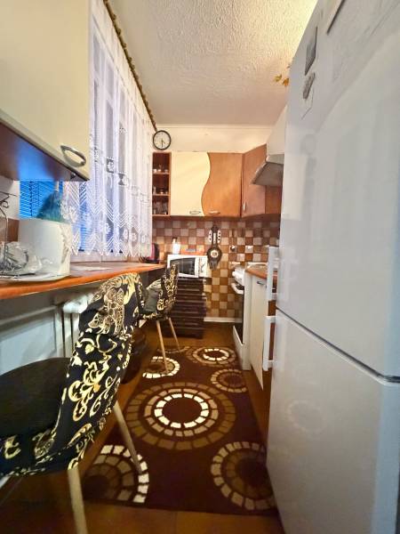 A kitchen in a 2-room apartment with a decorative rug, stools, and a tiled wall.
