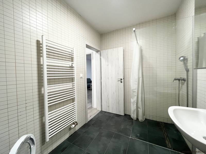 A bathroom in a studio apartment with dark tiles and a ladder radiator.