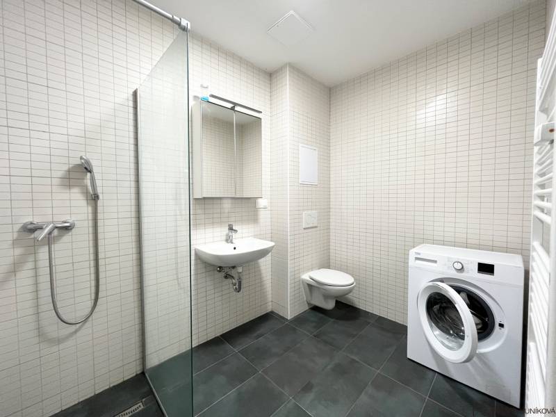 Bathroom in a studio apartment with a washing machine, shower, sink, and toilet.