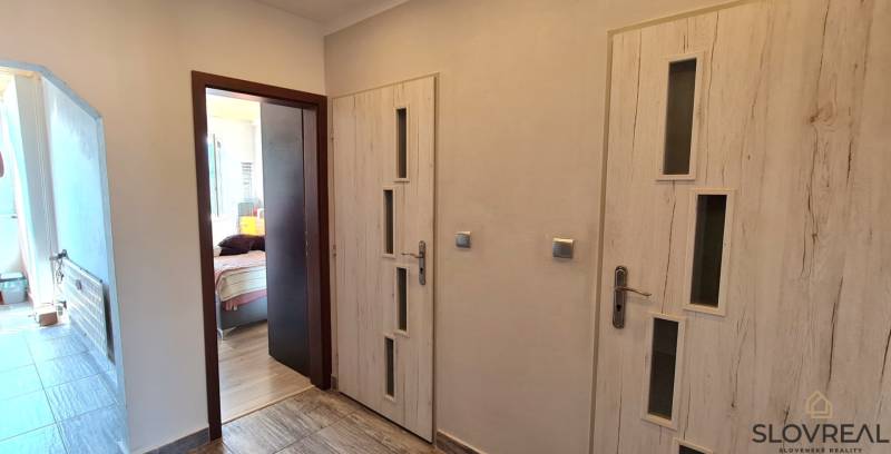 A hallway with doors in a 2-room apartment, floor with wooden decor, room on the left.