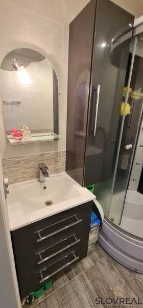 Bathroom in a 2-room apartment with a sink and a shower, decorative tiles on the wall.