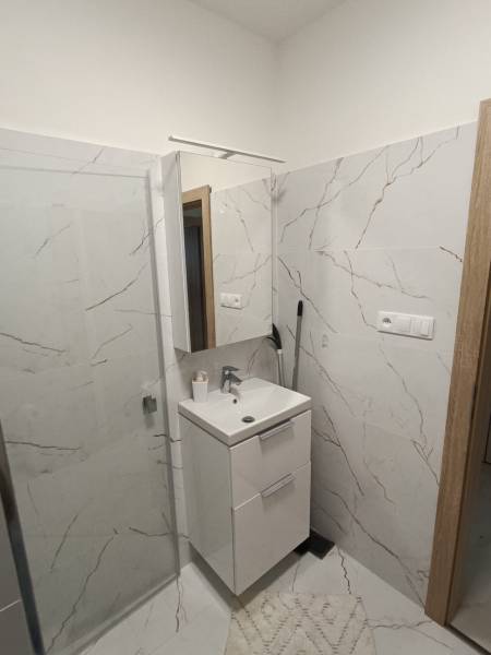 Bathroom with a sink, shower corner, and marble imitation tiles in a 2-room apartment.