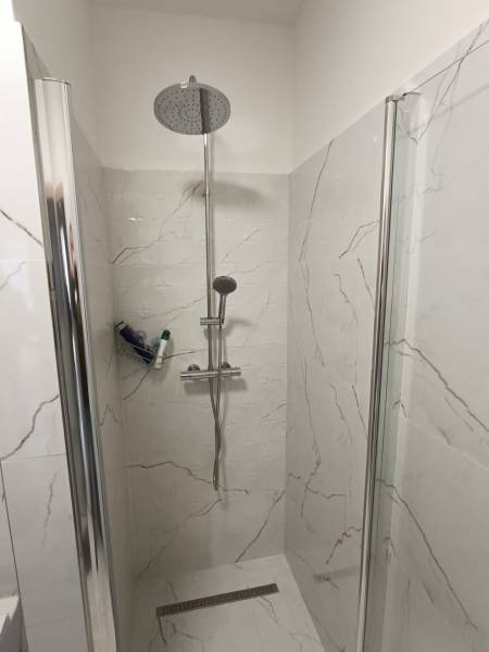 A shower enclosure with marble tiles in a 2-room apartment.