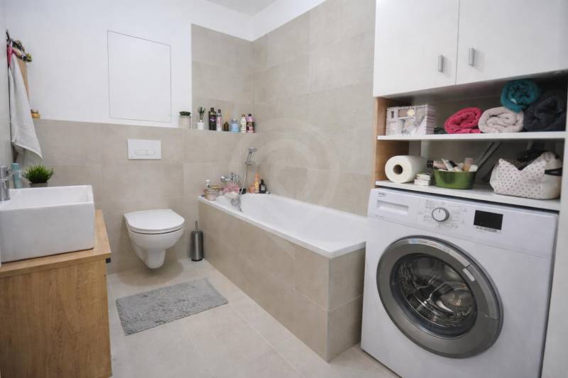 A bathroom in a studio apartment with a bathtub, washing machine, and toilet, complemented by storage space.