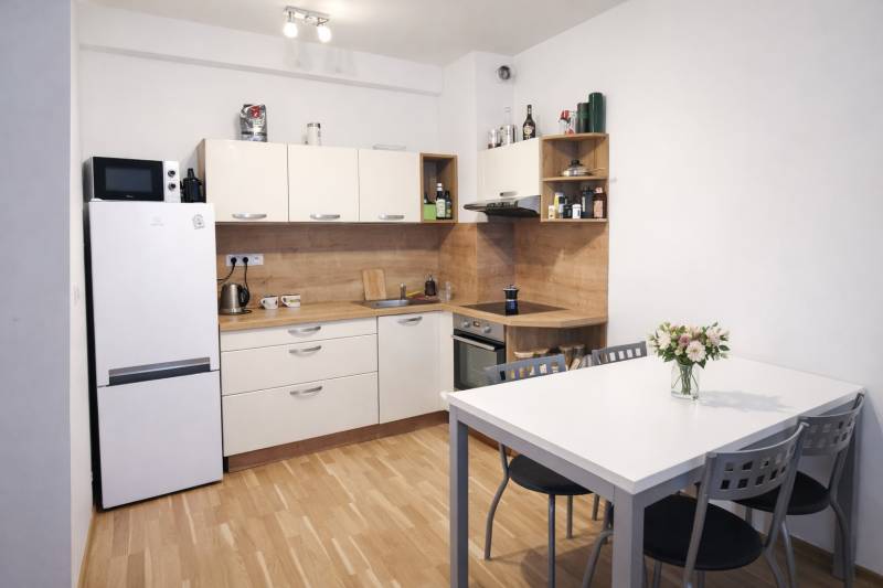 A kitchen in a 2-room apartment with a refrigerator, table, and wooden decor flooring.