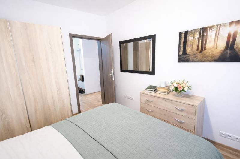 Bedroom in a two-room apartment with a wardrobe, dresser, and wooden decor flooring.