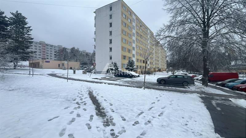 A winter scene on Bazovského Street in Zvolen with an apartment building and parked cars.
