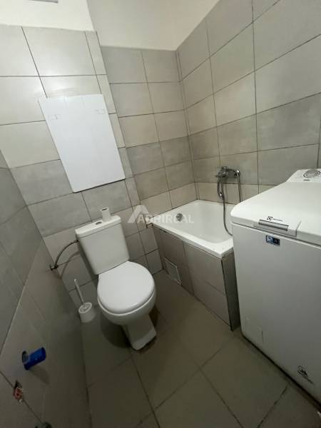 Bathroom of a one-room apartment with a washing machine, bathtub, and toilet.