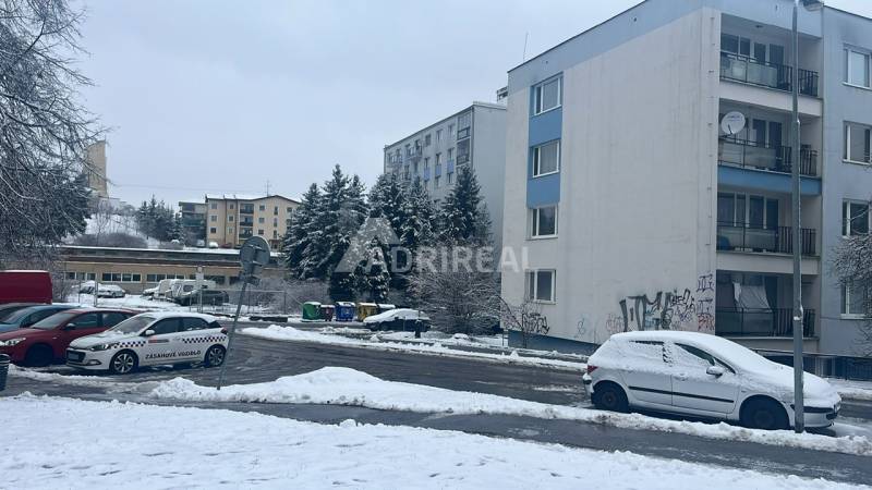 A snowy Bazovského street in Zvolen with parked cars next to a multi-story building.
