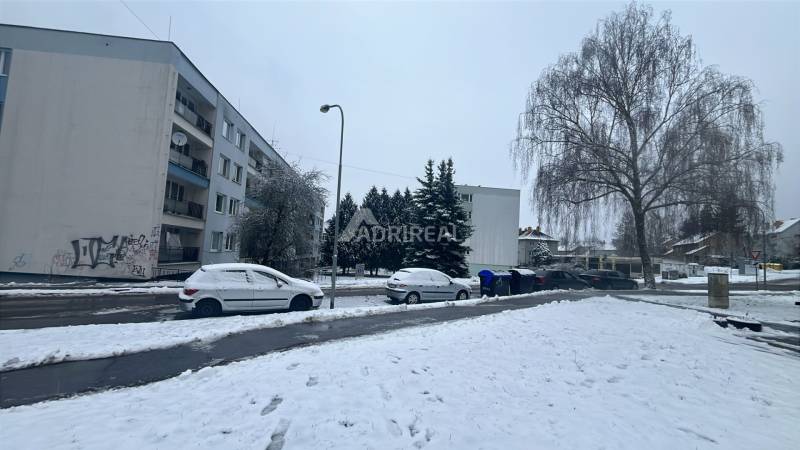 Winter street Bazovského in Zvolen with snow-covered cars and trees, apartment building in the background.