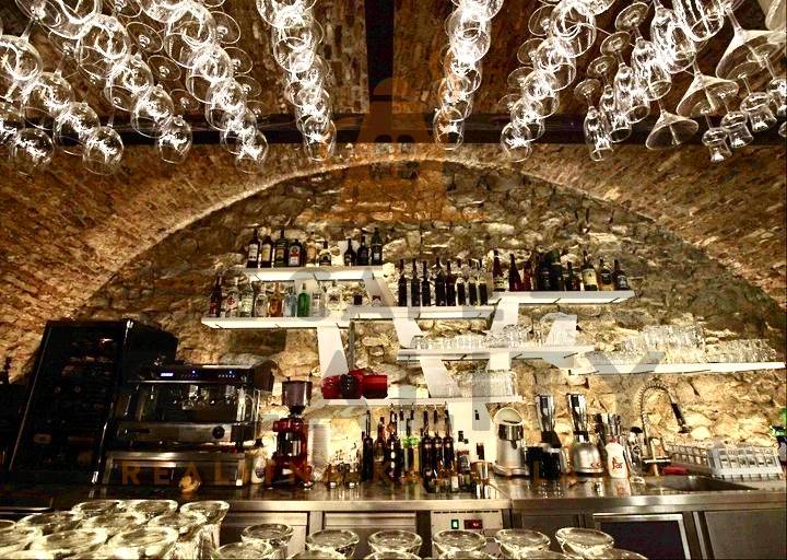 A bar with a vaulted ceiling, hanging glasses, stone decor, and alcohol in a gastro space.