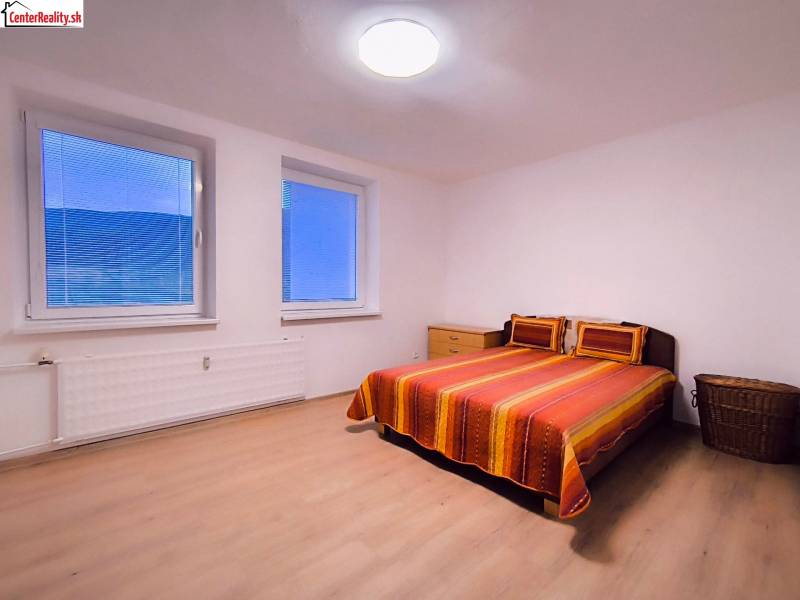 Bedroom in a two-room apartment with a double bed, wood-patterned flooring, and simple furniture.