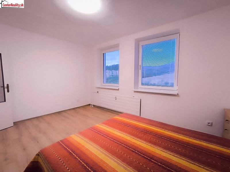 A bright room with two windows, a bed, and a floor with a wooden decor.