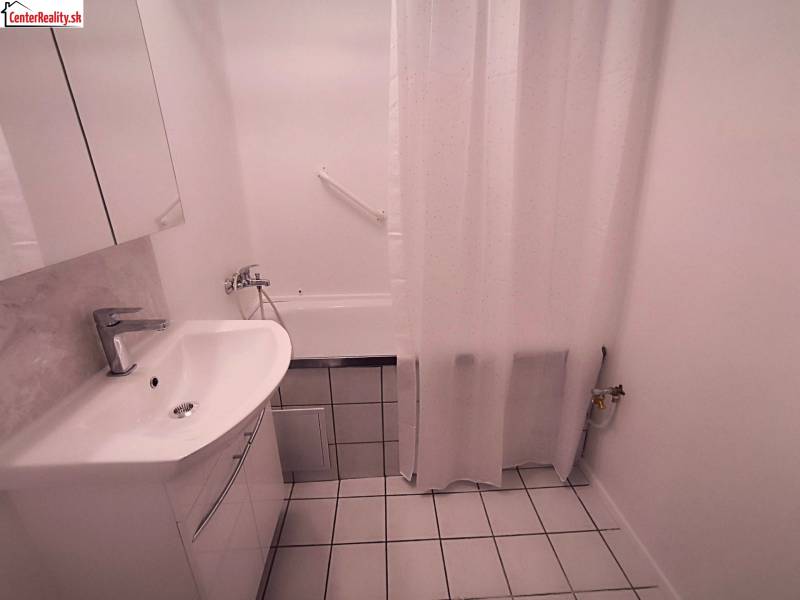 Bathroom in a 2-room apartment with a white sink, bathtub, and white tiles.