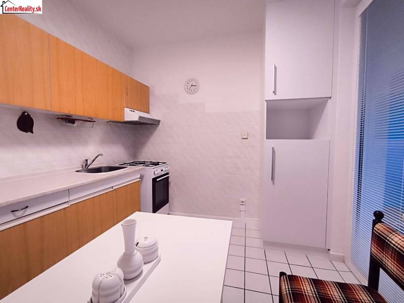 A kitchen in a 2-room apartment with tiles and light kitchen cabinets.