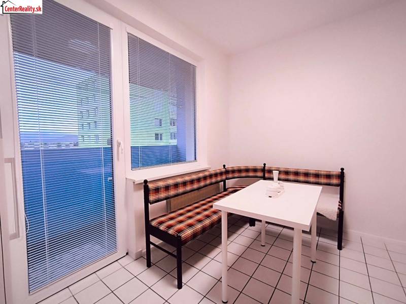 Dining nook with white tiles, a window, and a corner bench in a two-room apartment.