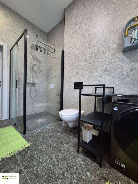 A bathroom in a studio apartment with a shower, a washing machine, and a storage rack.