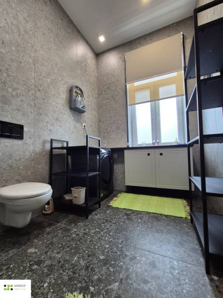 Bathroom in a studio apartment with a washing machine, toilet, and gray tiles.