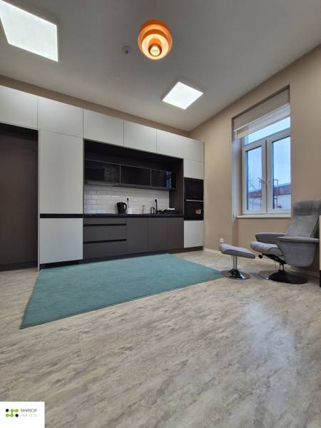 A kitchenette with white cabinets and a carpet in a studio apartment, wooden decor flooring.