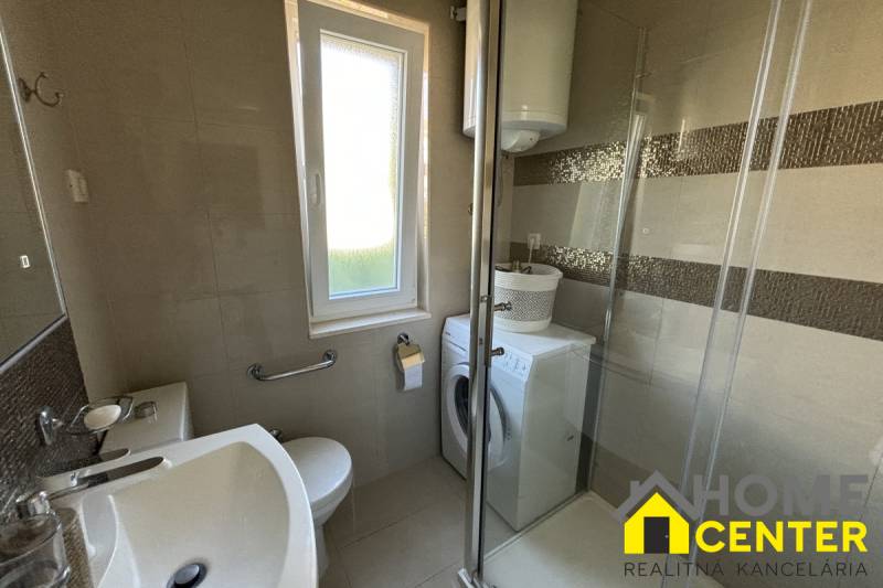 A bathroom in a family house with a shower, a washing machine, and a window.