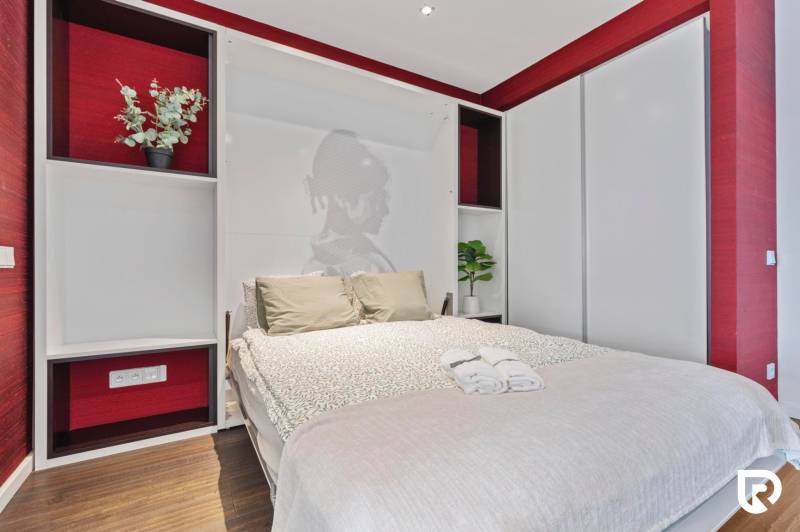 Bedroom with a decorative wall, bed, and storage space in a two-room apartment, floor with wooden decor.