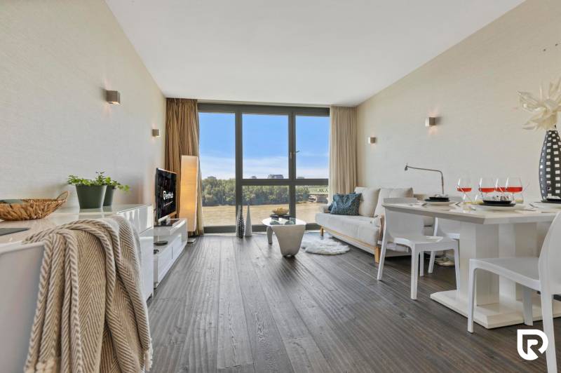 A stylish living room in a two-room apartment with a wooden decor floor and large windows.