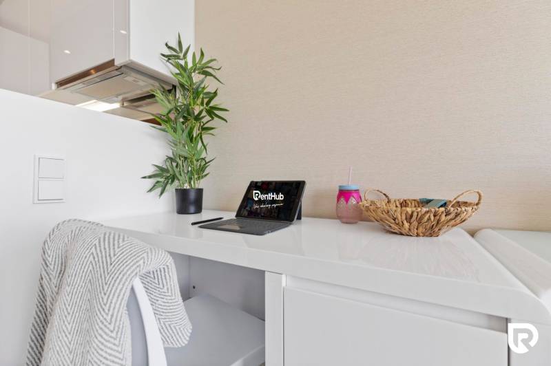 A workspace with a white desk, a laptop, a plant, and a blanket in a 2-room apartment.
