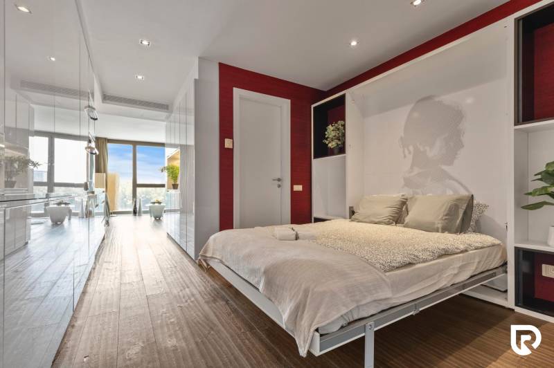 Bedroom with a bed, plants, and a wooden decor floor in a 2-room apartment.