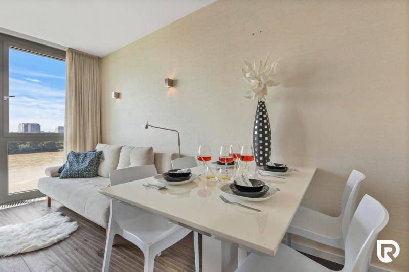 Dining area in a 2-room apartment with a sofa and wood-patterned flooring.