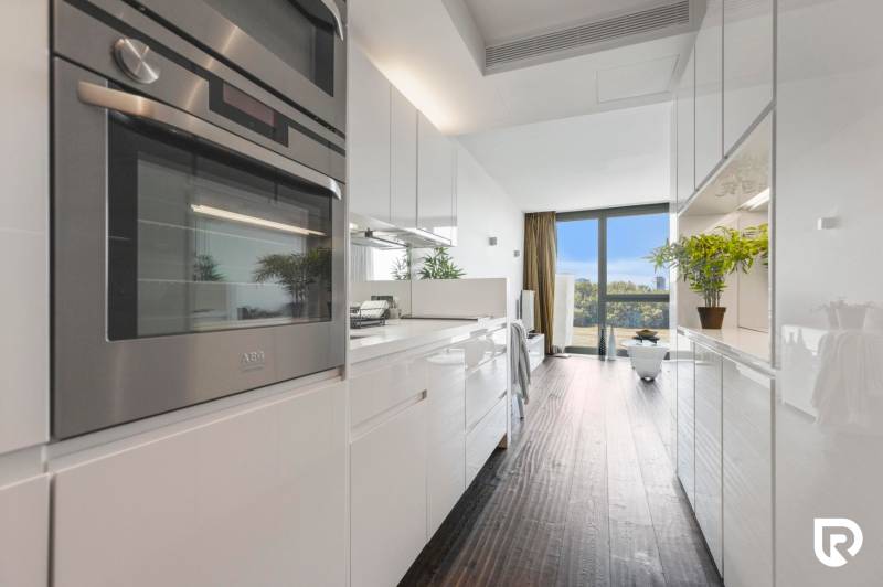 A kitchen in a 2-room apartment with glossy white cabinets and a floor with a wood decor.