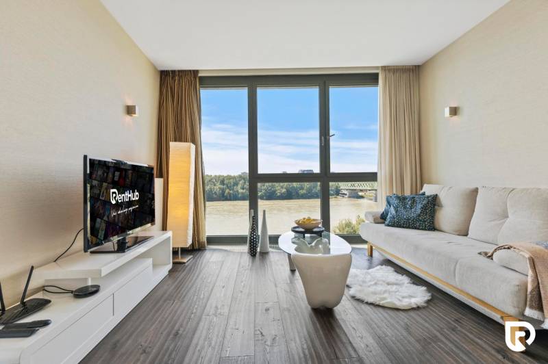 Living room in a two-room apartment with a view of the river, large window, wooden decor flooring.