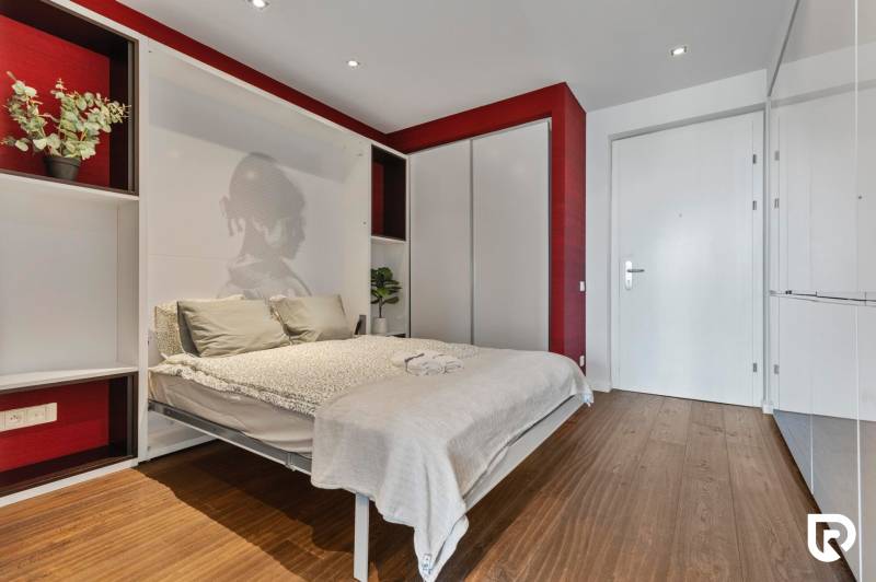 Bedroom in a 2-room apartment with wood-patterned flooring, red walls, built-in wardrobes.