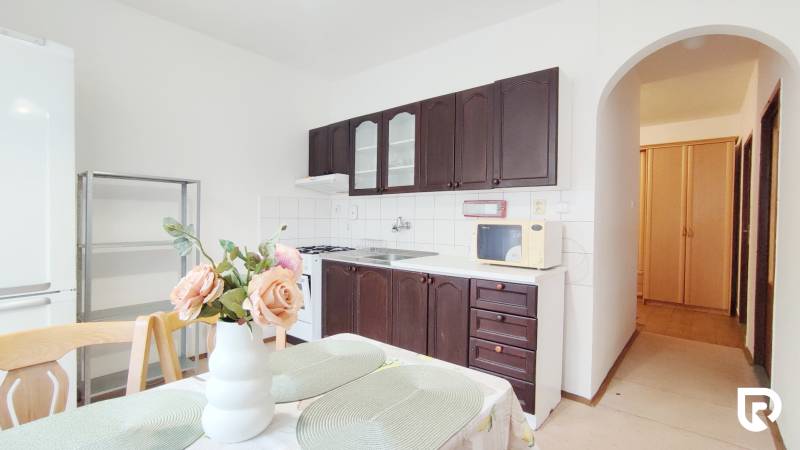 A kitchen in a 2-room apartment with dark cabinets and a dining table with decoration.