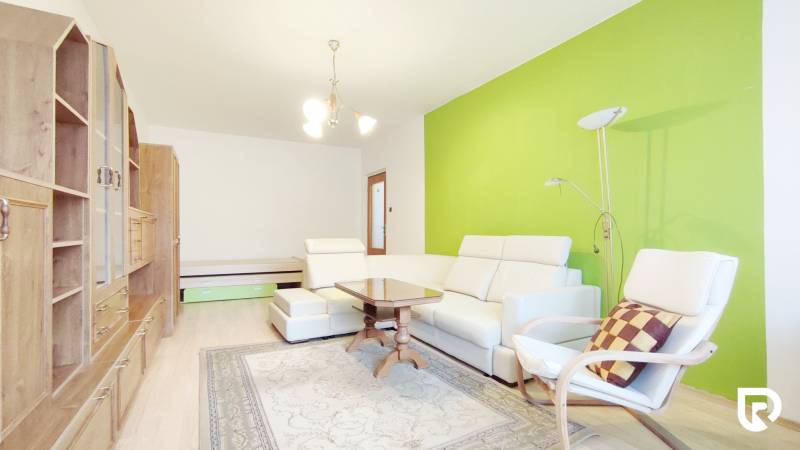 Living room in a two-room apartment with white furniture, a green wall, and a floor with a wooden decor.
