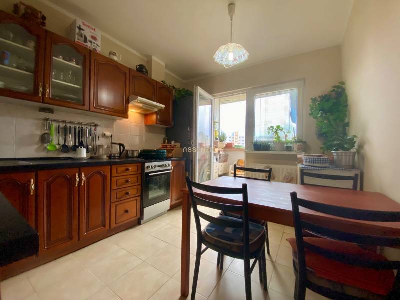 A kitchen in a 3-room apartment with wooden cabinets, a dining table, and a window to the balcony.