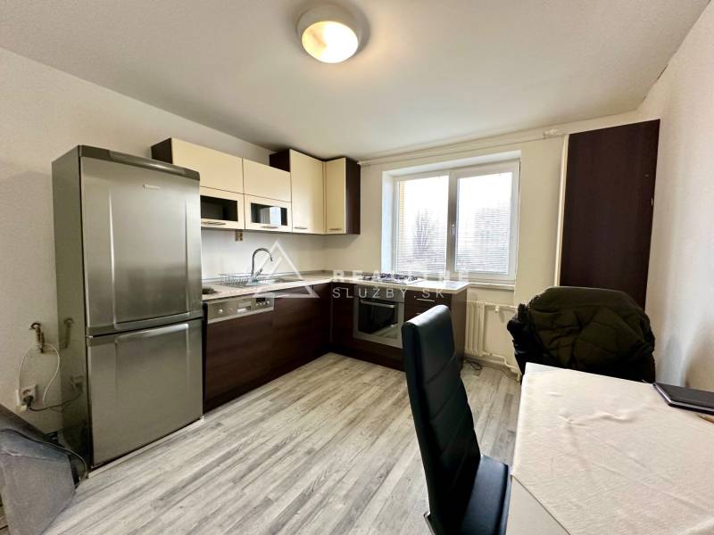 A kitchen in a 2-room apartment with a wooden decor floor and a table with chairs.