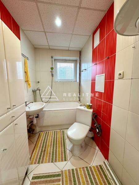 Bathroom in a 2-room apartment with a bathtub, sink, and white tiles.