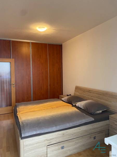 Bedroom in a two-room apartment with a bed and a wardrobe, floor with wooden decor.