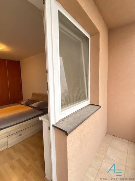 Bedroom in a two-room apartment with a bed, wooden decor flooring, and access to the terrace.