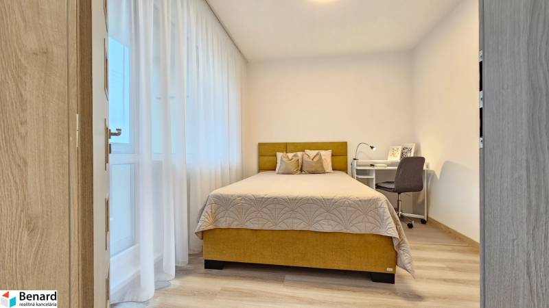 Bedroom in a studio apartment with a bed, a desk, and a wooden decor floor.
