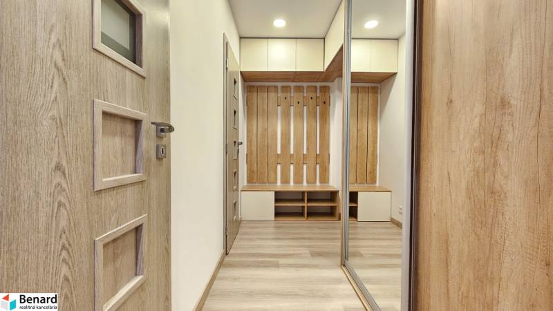 Interior of a 1-room apartment with a wooden decor floor, cabinets, and a coat rack wall.