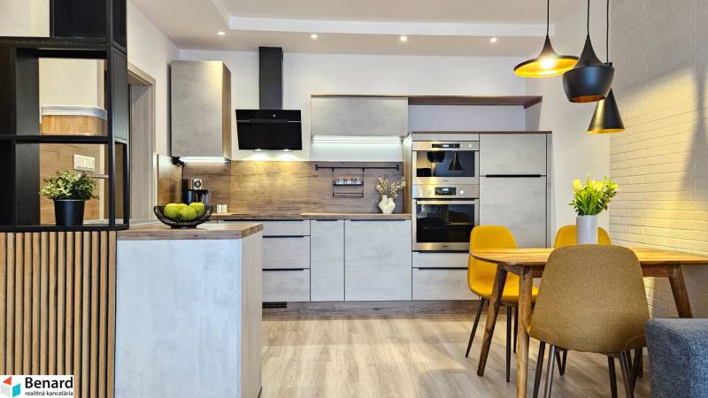 A kitchen in a studio apartment with a wood-patterned floor, a dining table, and yellow chairs.