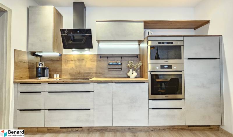 A kitchen unit in a studio apartment with a wooden decor, appliances, and lighting.