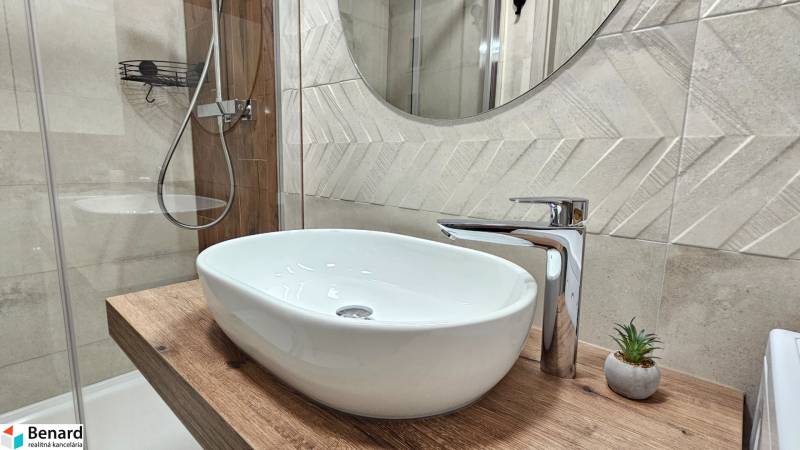 Bathroom in a studio apartment with a sink on wooden decor and a modern faucet.