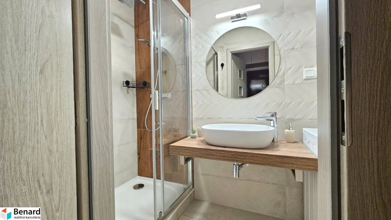 Bathroom in a studio apartment with a round mirror, shower, and wooden decor.